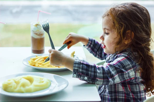 Niña almorzando en el restaurante con el cuchillo de mesa y tenedor en las manos. — Foto de Stock