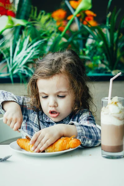 Aranyos kislány reggelizik a croissant egy étteremben. — Stock Fotó