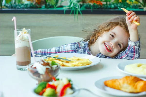 Niña comiendo papas fritas en un restaurante . — Foto de Stock