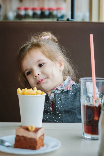 Niña en un restaurante comiendo papas fritas y bebiendo cola. — Foto de Stock
