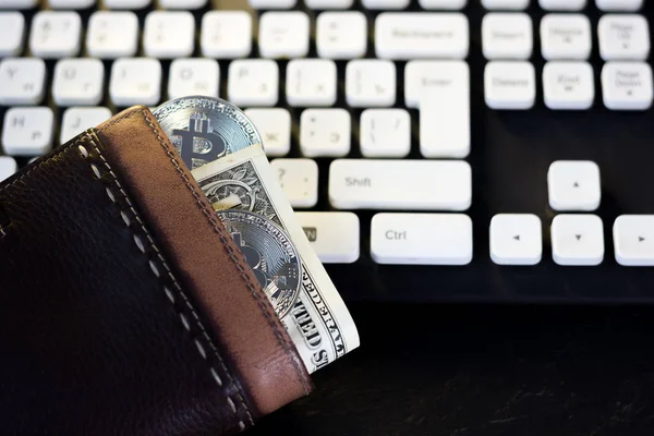 Wallet with cash and bitcoin coin over the computer keyboard