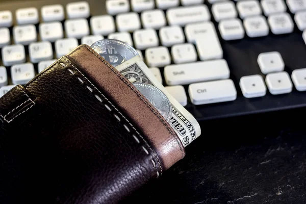 Wallet with cash and bitcoin coin over the computer keyboard