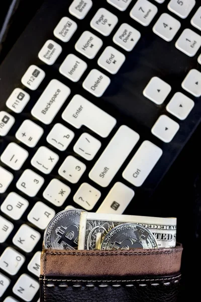 Wallet with cash and bitcoin coin over the computer keyboard