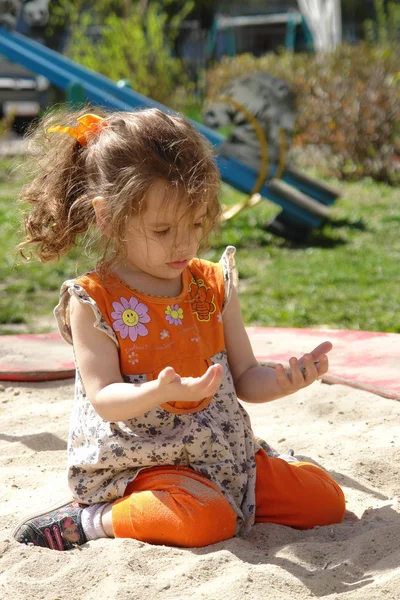 Kid girl playing in a sandpit on a summer day