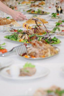 Yemek masası. Elinde maşayla yemek yiyor.