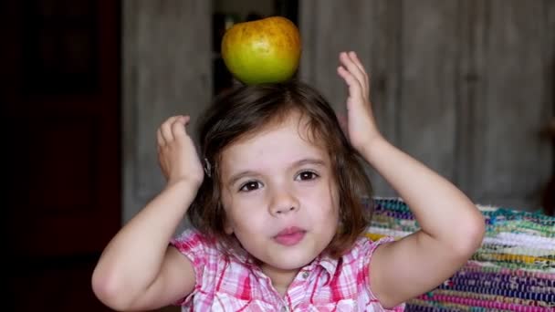 Πλάνα Αξιολάτρευτο Κοριτσάκι Κρατώντας Μήλο Στο Κεφάλι Στο Σπίτι — Αρχείο Βίντεο