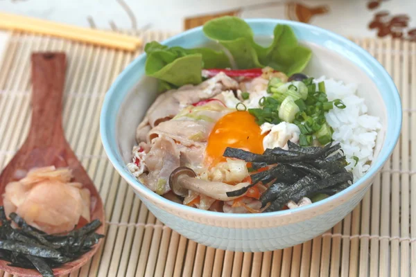 Nahaufnahme von Jasminreis wird mit weich gekochten Eiern und gebratenem Schweinefleisch im japanischen Stil als "oyakodon" mit Beilage als getrocknetes Algenblatt und eingelegtem Ingwer belegt. Selektiver Fokus. — Stockfoto