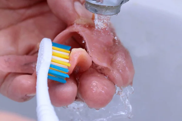 Utilizzare uno spazzolino da denti per pulire i denti protesi parziale . Immagine Stock