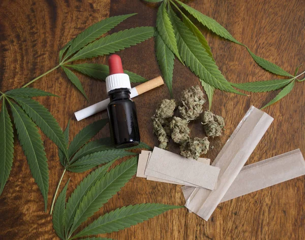 Cannabis sativa ogräs blad och blomma knopparna på trä bakgrund med Thc olja, cigarett och röka papper — Stockfoto