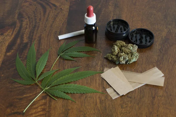 Cannabis sativa folhas de ervas daninhas e botões de flores em fundo de madeira com moedor e grande papel para fumar — Fotografia de Stock