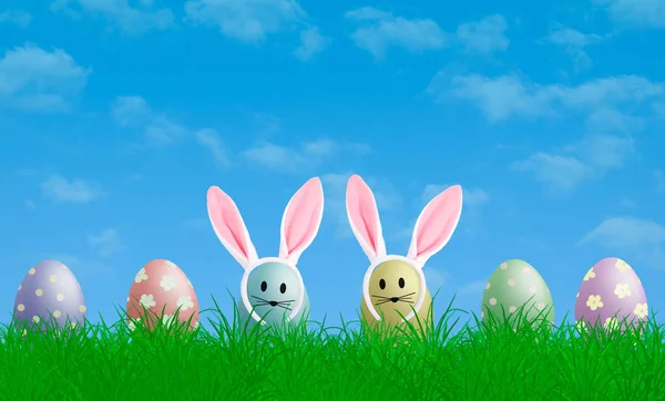 Colorful pastel easter eggs with bunny ears in grass with blue sky background, copy space — Stock Photo, Image