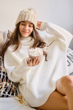 Evde dinlenin. Genç bir kız elinde bir fincan kakaoyla yatakta oturuyor.. 