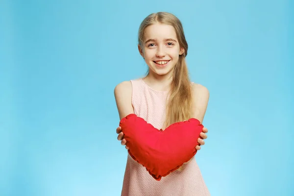 Маленькая девочка и сердце. Веселая маленькая девочка с сердцем из ткани на синем фоне . — стоковое фото