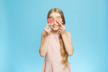 İzole edilmiş küçük kız mavi arka plandaki kağıt kalplerle gözlerini kapatıyor. İzole edilmiş yarım boy portre.