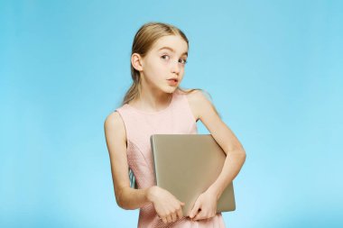 Bilgisayarı olan bir kız. Mavi arka planda izole edilmiş sarışın kız elinde bir bilgisayar tutuyor..