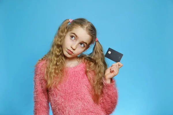 Маленькая девочка с банковской картой. Радостная девушка изолирована на синем фоне. Концепция сбережений, вкладов . — стоковое фото