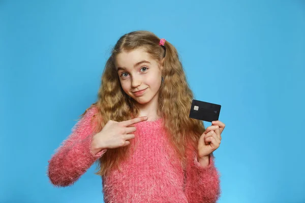 Banka kartı olan küçük bir kız. Mavi arka planda izole edilmiş neşeli bir kız. Tasarruf ve depozito kavramı. — Stok fotoğraf