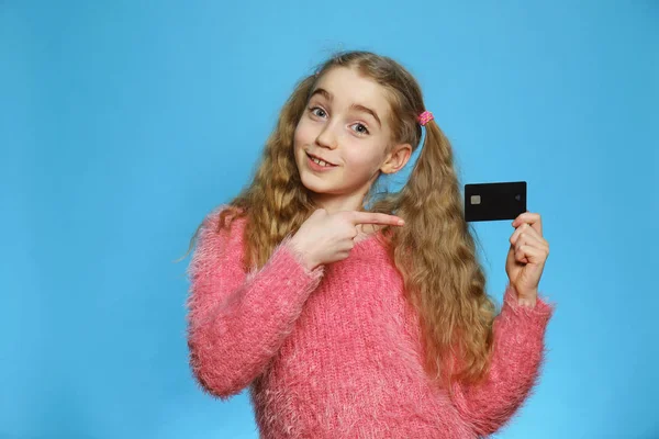 Маленькая девочка с банковской картой. Радостная девушка изолирована на синем фоне. Изолированный полудлинный портрет . — стоковое фото