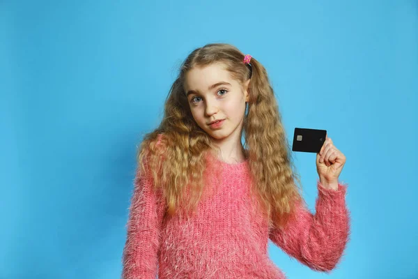 Kleines Mädchen mit einer Bankkarte. fröhliches Mädchen isoliert auf blauem Hintergrund. Einzelnes Halblanges Porträt. — Stockfoto