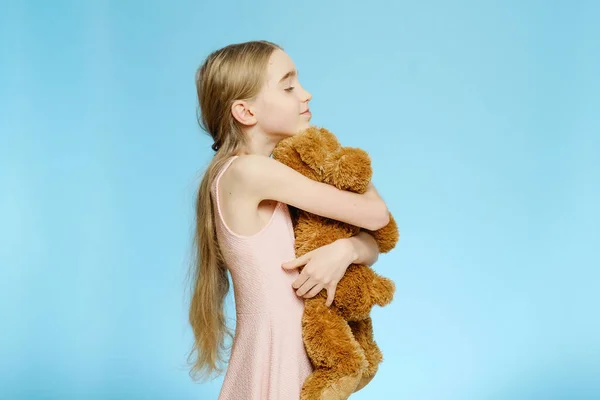 Girl hugs a big teddy bear. Isolated portrait on a blue background. Children\'s joy