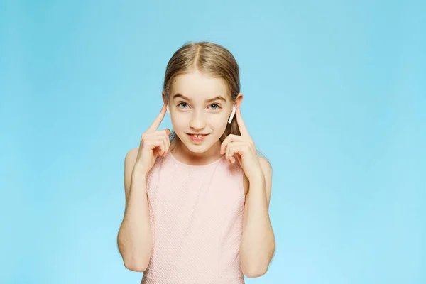 Schöne kleine Mädchen hört Musik durch drahtlose Kopfhörer. Mädchen blickt in die Kamera. Porträt auf blauem Hintergrund. — Stockfoto