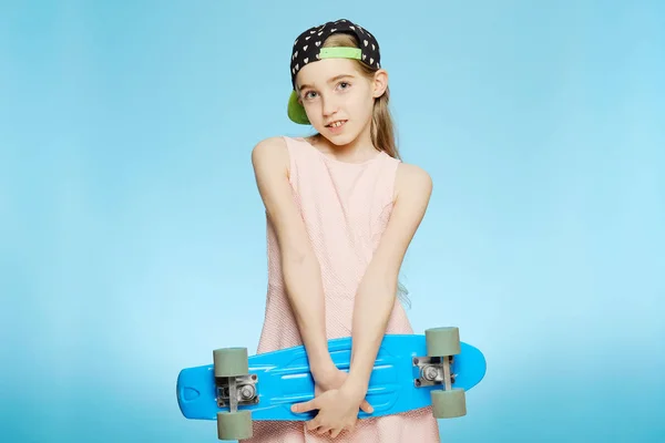 Девушка-подросток держит синий скейтборд в руках студии. Изолированный портрет студии на синем фоне — стоковое фото