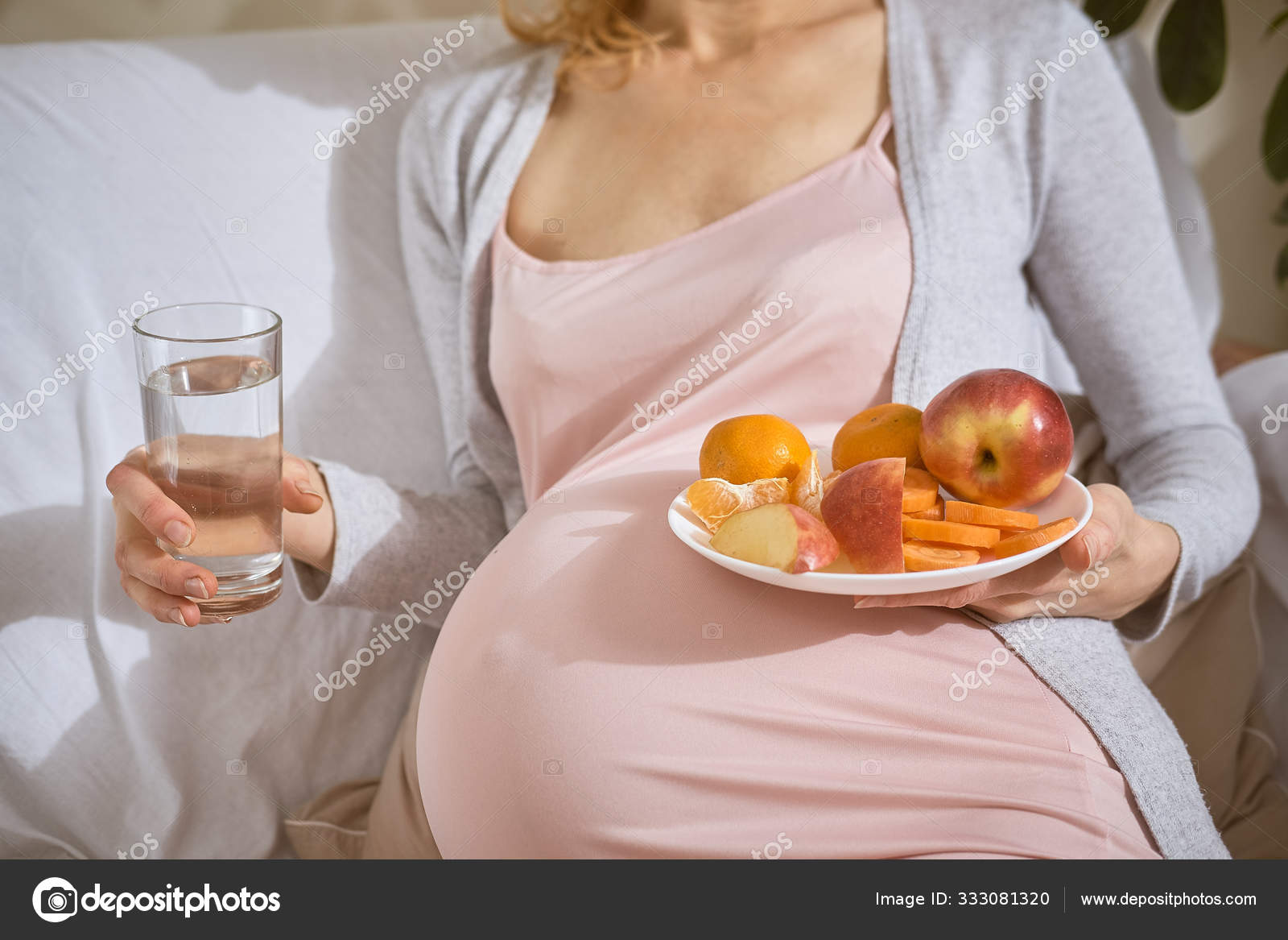 Pregnant belly and food. In her hands a woman holds a glass of water