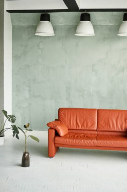 Loft style interior. Orange sofa in the interior and white lamps on the ceiling.