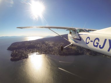 Tofino, Vancouver Island, British Columbia, Canada - June 29, 2017 - Small Cessna 172 Airplane Flying around the city on Pacific Coast during a bright sun clipart