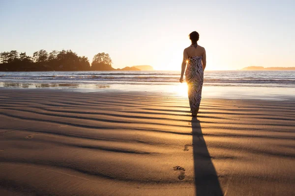 Rear view of the woman walking in the water of the ocean at sunset time