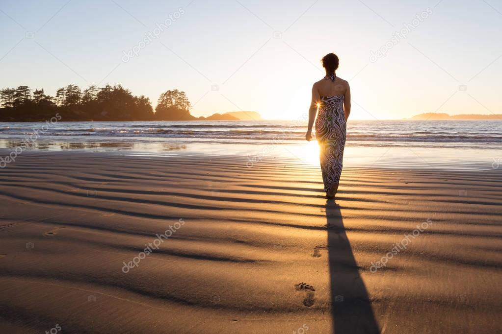 Rear view of the woman walking in the water of the ocean at sunset time 
