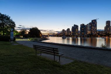 Bench in a park at False Creek with Downtown Vancouver, BC, Canada, in the background during sunset. clipart