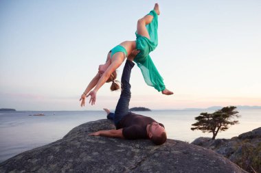 Genç insanlar, erkek ve kadın, güzel bir çift yapıyorsun Acro Yoga birlikte doğada bir renkli yaz gün batımı sırasında. Whytecliff Park, Horseshoe Bay, Batı Vancouver, Bc, Kanada içinde alınan.