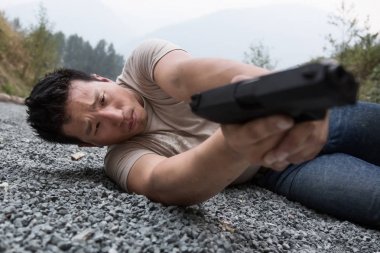 Asya genç adamdır çakıl zemin döşeme pozisyon tutan bir tabanca ve bir silah mesafeden ateş amaçlayan.