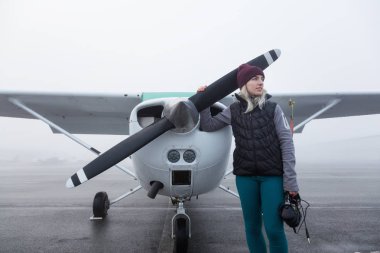 Genç beyaz kadın öğrenci Pilot havaalanında tek bir motor uçağın önünde duruyor. Pitt Meadows, Vancouver, Bc, Kanada sisli kış sabah sırasında alınan.