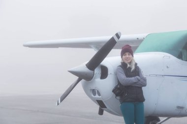 Genç beyaz kadın öğrenci Pilot havaalanında tek bir motor uçağın önünde duruyor. Pitt Meadows, Vancouver, Bc, Kanada sisli kış sabah sırasında alınan.