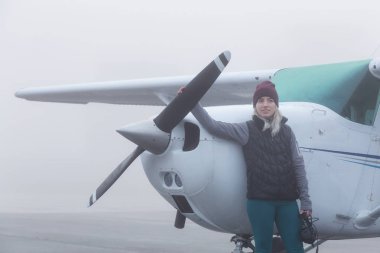 Genç beyaz kadın öğrenci Pilot havaalanında tek bir motor uçağın önünde duruyor. Pitt Meadows, Vancouver, Bc, Kanada sisli kış sabah sırasında alınan.