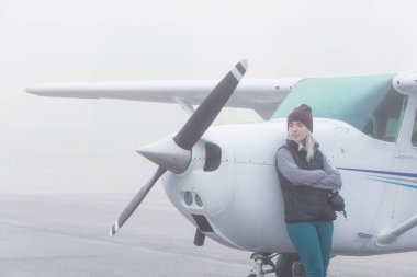 Genç beyaz kadın öğrenci Pilot havaalanında tek bir motor uçağın önünde duruyor. Pitt Meadows, Vancouver, Bc, Kanada sisli kış sabah sırasında alınan.