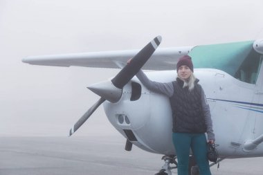 Genç beyaz kadın öğrenci Pilot havaalanında tek bir motor uçağın önünde duruyor. Pitt Meadows, Vancouver, Bc, Kanada sisli kış sabah sırasında alınan.