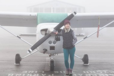 Genç beyaz kadın öğrenci Pilot havaalanında tek bir motor uçağın önünde duruyor. Pitt Meadows, Vancouver, Bc, Kanada sisli kış sabah sırasında alınan.