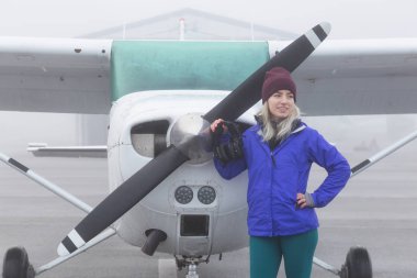 Genç beyaz kadın öğrenci Pilot havaalanında tek bir motor uçağın önünde duruyor. Pitt Meadows, Vancouver, Bc, Kanada sisli kış sabah sırasında alınan.
