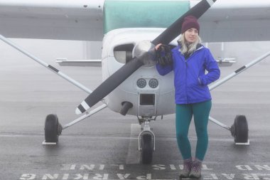 Genç beyaz kadın öğrenci Pilot havaalanında tek bir motor uçağın önünde duruyor. Pitt Meadows, Vancouver, Bc, Kanada sisli kış sabah sırasında alınan.