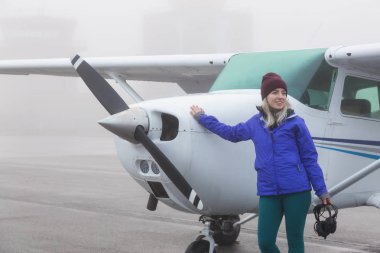 Genç beyaz kadın öğrenci Pilot havaalanında tek bir motor uçağın önünde duruyor. Pitt Meadows, Vancouver, Bc, Kanada sisli kış sabah sırasında alınan.