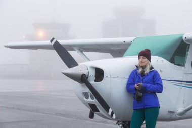Genç beyaz kadın öğrenci Pilot havaalanında tek bir motor uçağın önünde duruyor. Pitt Meadows, Vancouver, Bc, Kanada sisli kış sabah sırasında alınan.