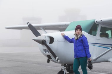 Genç beyaz kadın öğrenci Pilot havaalanında tek bir motor uçağın önünde duruyor. Pitt Meadows, Vancouver, Bc, Kanada sisli kış sabah sırasında alınan.