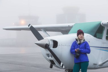 Genç beyaz kadın öğrenci Pilot havaalanında tek bir motor uçağın önünde duruyor. Pitt Meadows, Vancouver, Bc, Kanada sisli kış sabah sırasında alınan.