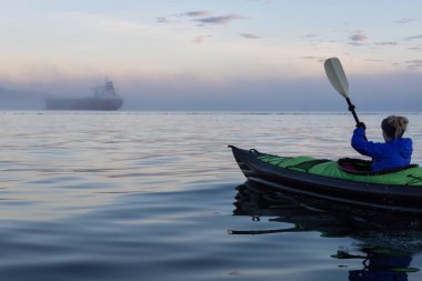 Macera kız Horseshoe Bay şişme bir kayık içinde belgili tanımlık geçmiş bir gemi üzerinde kayak. Vancouver, Bc, Kanada, bir kış aylarında günbatımı alınan.