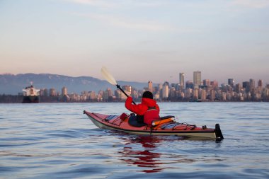 Deniz kayağı macera adamın paddline arka planda şehir merkezinde şehir manzarası ile bir canlı kış günbatımı sırasında olur. Vancouver, British Columbia, Kanada alınan.