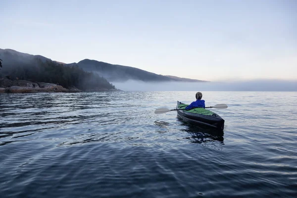 Adventurous woman is sea kayaking on an inflatable kayak during a vibrant winter sunset. Taken in Horseshoe Bay, West Vancouver, BC, Canada. Concept: adventure, holiday, vacation, explore