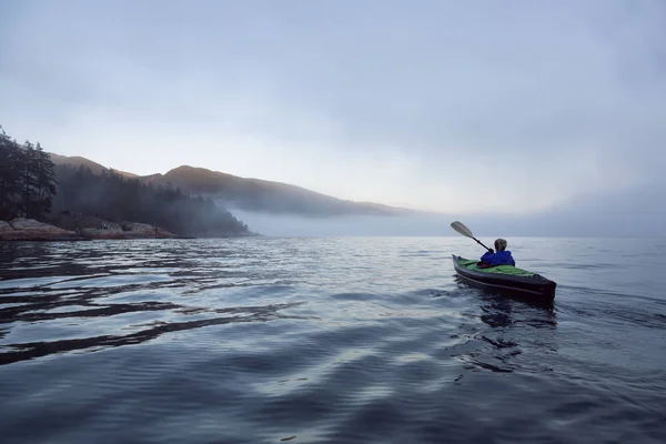 Adventurous woman is sea kayaking on an inflatable kayak during a vibrant winter sunset. Taken in Horseshoe Bay, West Vancouver, BC, Canada. Concept: adventure, holiday, vacation, explore